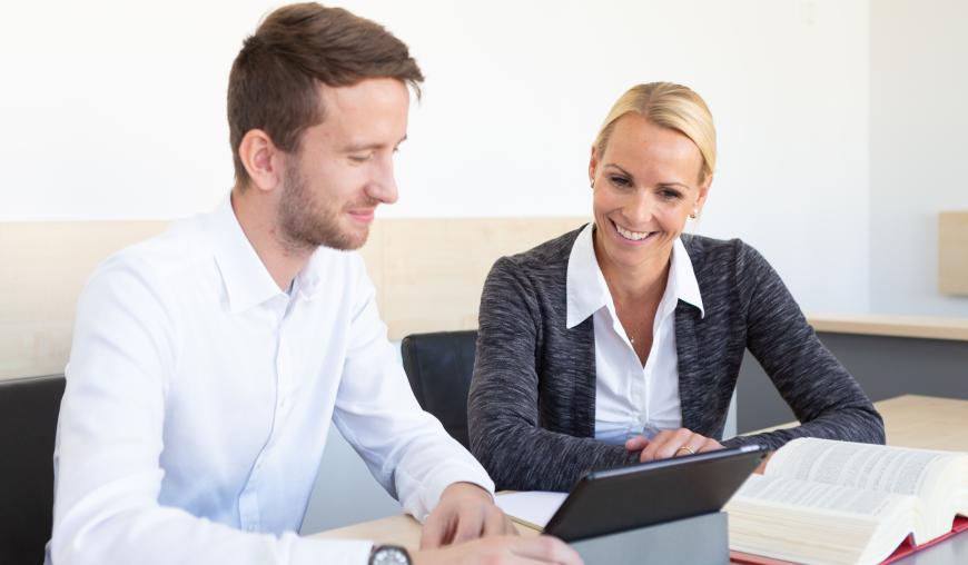 Eine Frau und ein Mann beugen sich gemeinsam über einen Laptop. Vor ihnen liegt ein Gesetzestext.